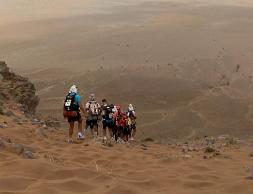 Runners traversing a large rocky sand dune in the desert. 