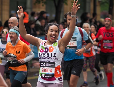 London Marathon runner wearing a Royal Marsden Cancer Charity vest, smiling at the crowd with her arms up