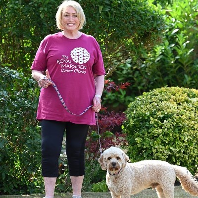 Woman in a pink Royal Marsden t-shirt standing outside with her dog next to her on a lead