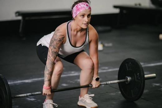 A person in gym clothing squatting down, about to lift a large weight