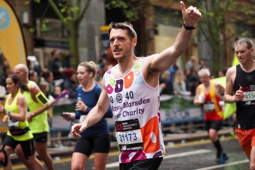 A man running a marathon, wearing a Royal Marsden Cancer Charity running vest and putting his thumbs up