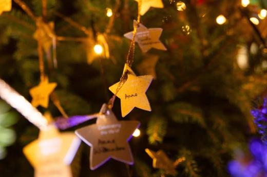 A string of gold stars on a Christmas tree. The middle star is in focus and has 'Anne' hand written on it. 