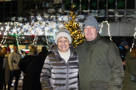 Rebecca Gallagher and her husband stand in front of a Christmas tree, smiling.