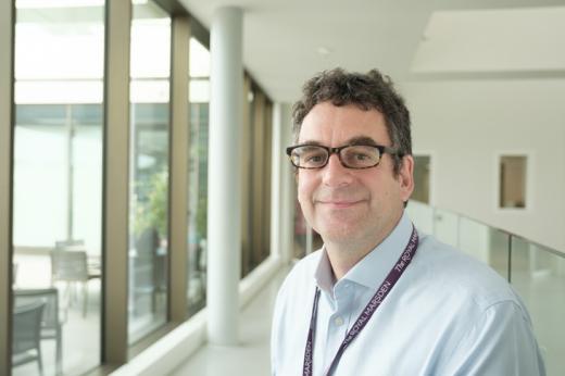 Man smiling, wearing glasses, in front of long window