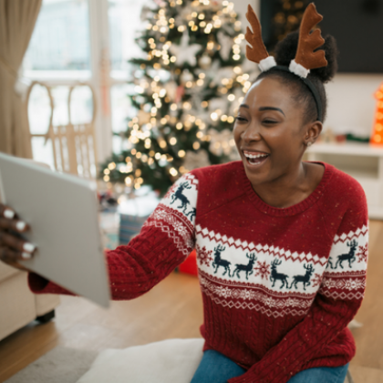 Image of a smiley, young black woman wearing a Christmas jumper and holding a virtual call by using her tablet.