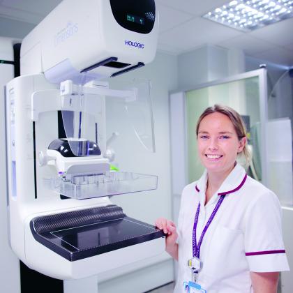 A Nurse smiling standing beside a mammography machine