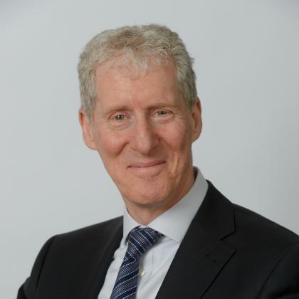 Portrait photo of Roger Gray. He is smiling and wearing a suit and tie. 