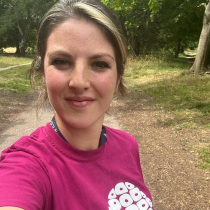 A selfie of a woman who is walking in the woods. She is smiling and wearing a Royal Marsden Cancer Charity t-shirt. 