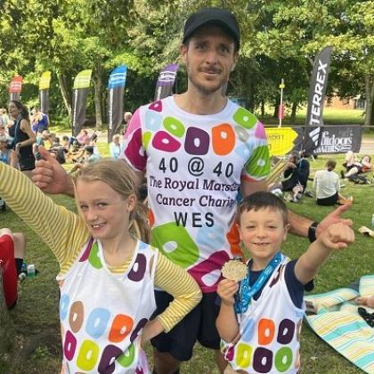Wes and his two children in Royal Marsden Cancer Charity-branded shirts. The kids are doing superman poses and his son his holding Wes's medal