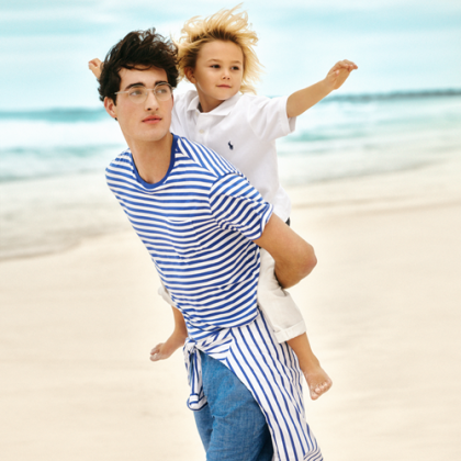 A man in a striped ralph lauren t-shirt holding a child on his back on a beach