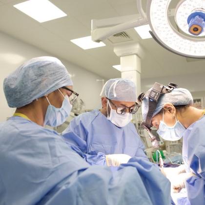 Three surgeons in scrubs and masks looking down and carrying out an operation