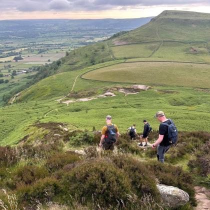 A group of four men hiking down a steep hill with a big landscape of hills in the background. 