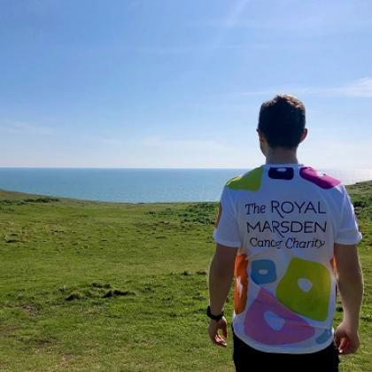 Back of trekker wearing Charity t-shirt, looking at the sea, hills and blue sky