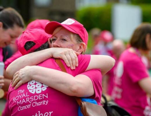 Two women wearing pink Banham Marsden March participant t-shirts and caps. They are hugging