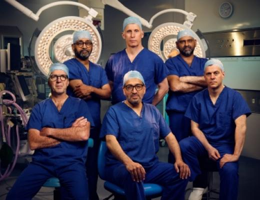 Six Royal Marsden surgeons in a group in a surgery theatre. They are wearing dark blue scrubs and surgery caps. 