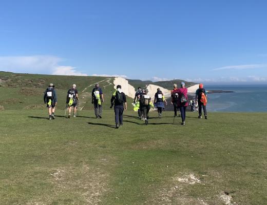 A group of Royal Marsden Cancer Charity fundraisers, walking across the stunning scenery of the South Downs - white chalk cliffs and a blue sea on a sunny day.