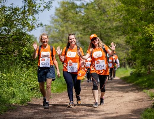 A group of three women in orange t-shirts and caps walking through woodland on The Banham Marsden March route