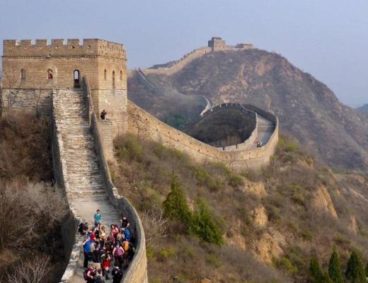 Panoramic view of Great Wall of China over mountains, with several walkers on the wall