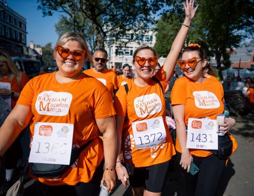 a group of women in orange Banham Marsden March t-shirts and matching orange heart-shaped glasses celebrating at the start line for the walk. 