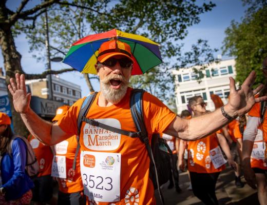 A man with a big white beard and an umbrella hat smiling with his arms out- the photo is fun and dynamic