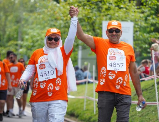 a couple in matching orange Banham Marsden March t-shirts and caps raise their arms in celebration at the finish line of The Banham Marsden March.