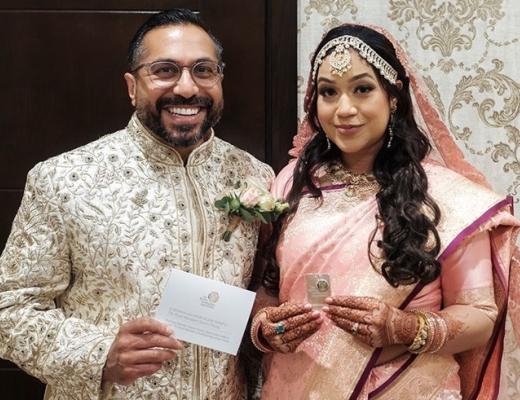 A man and a woman dressed in Indian wedding clothes, holding wedding favours